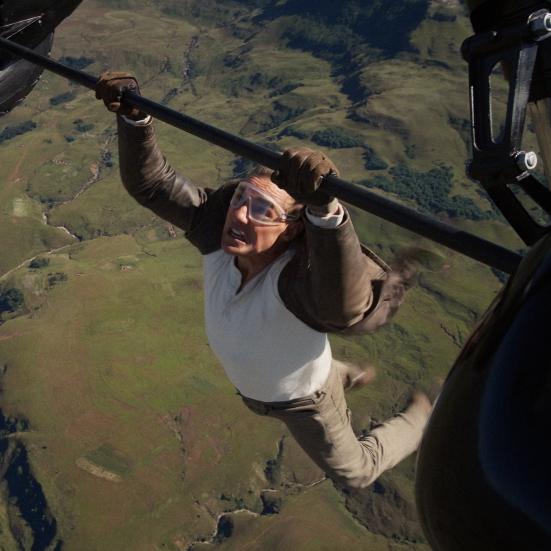 Tom Cruise hænger fra en flyvemaskine højt over jorden.