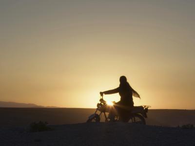 Billede af hovedpersonen fra filmen på en motorcykel i solnedgangen.